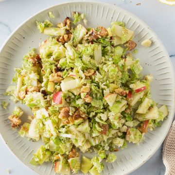 Roher Rosenkohlsalat mit Apfel und Waln&uuml;ssen auf einem Teller, Deko im Bildrand.