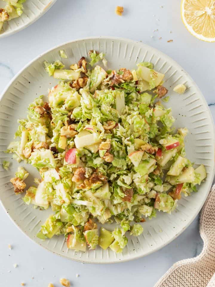 Roher Rosenkohlsalat mit Apfel und Waln&uuml;ssen auf einem Teller, Deko im Bildrand.