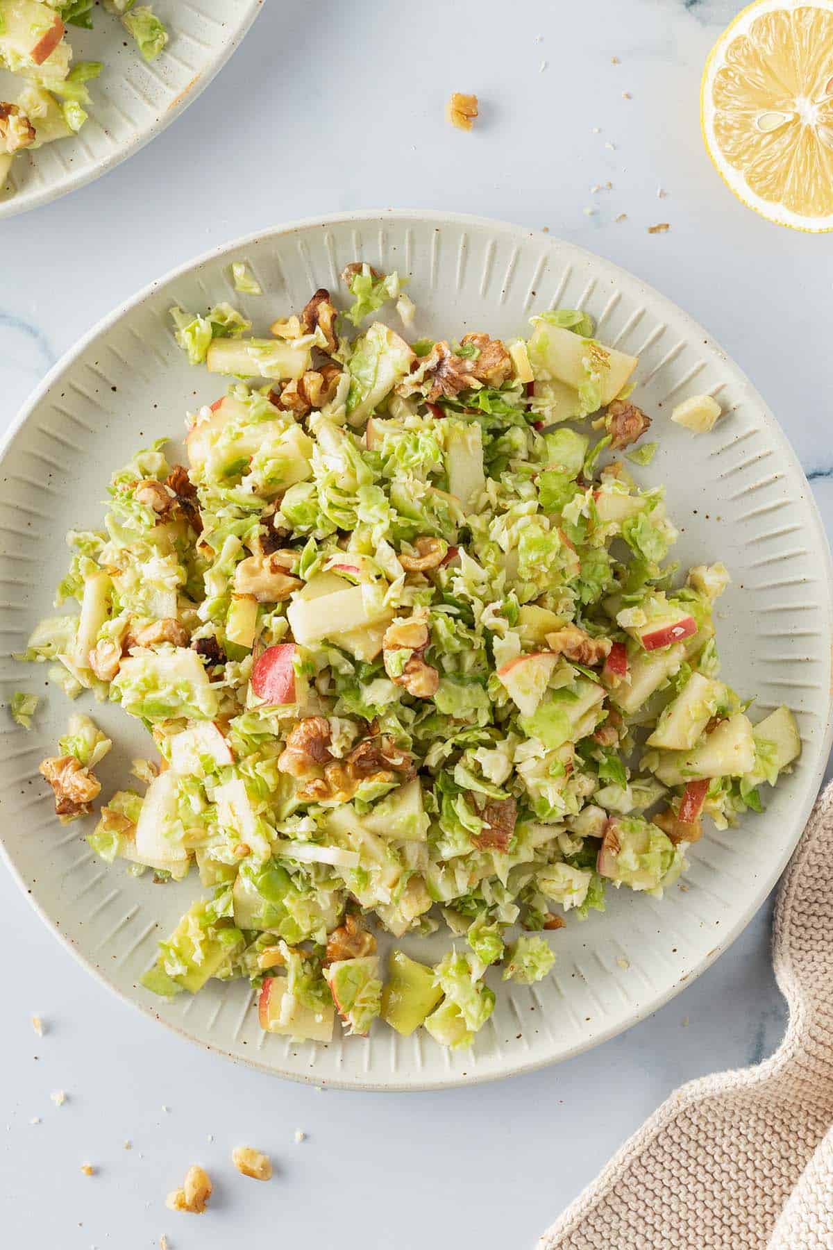Roher Rosenkohlsalat mit Apfel und Waln&uuml;ssen auf einem Teller, Deko im Bildrand.