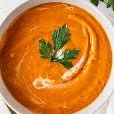 Cremige rote Linsensuppe mit Kokosmilch in einer Sch&uuml;ssel, dekoriert mit frischen Korianderbl&auml;ttern.