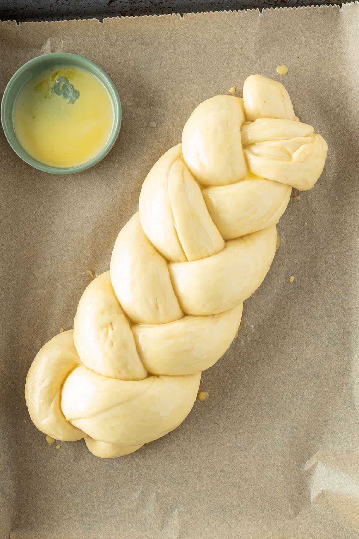 Der mit Eigelb bestrichene Hefezopf liegt auf einem Blech mit Backpapier.