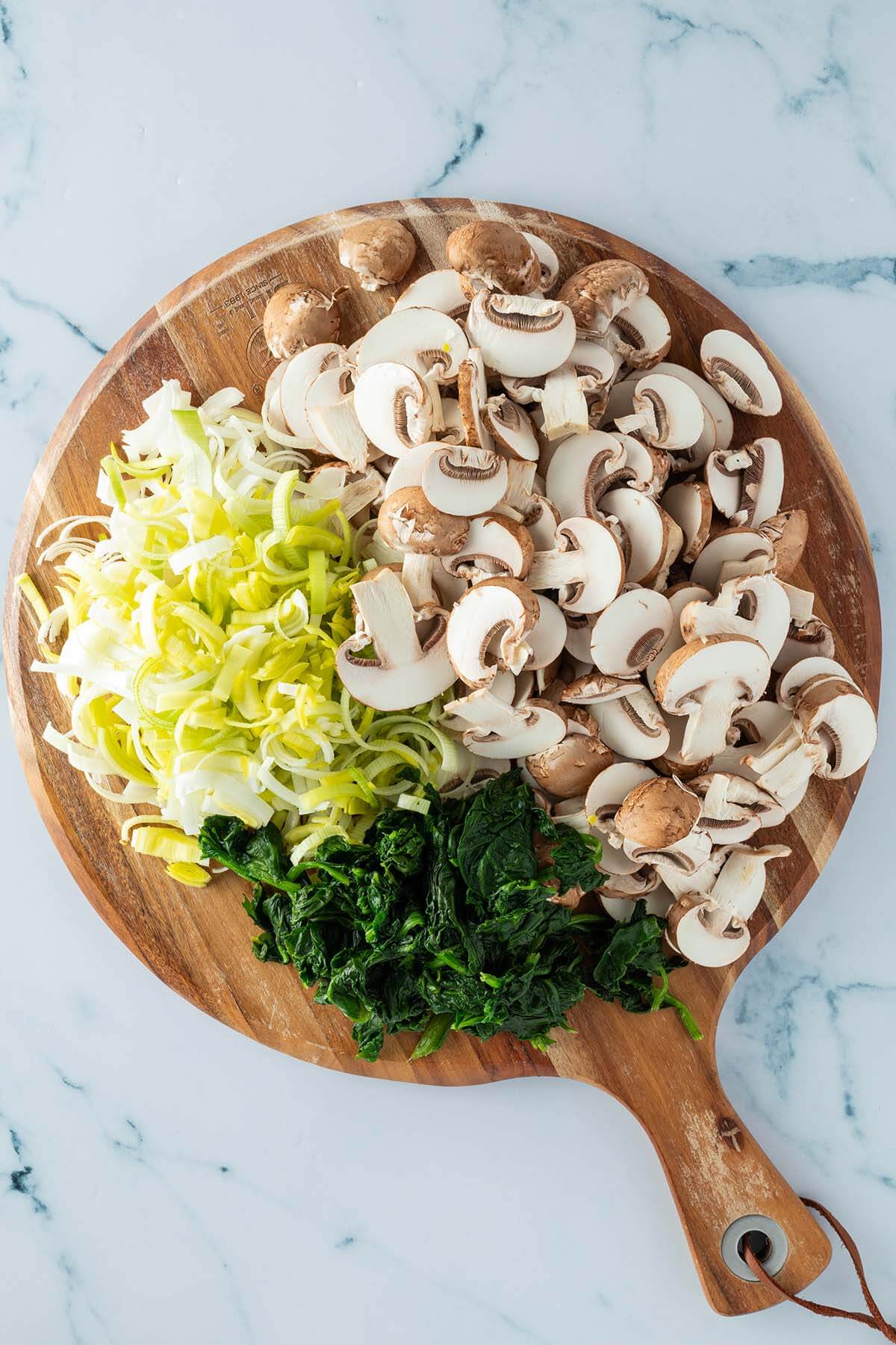 Klein geschnittene Champignons, Lauch und Spinat auf einem Brett.