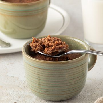 Schoko-Tassenkuchen in einer Kaffeetasse, zwei Kuchen und ein Glas Milch im Hintergrund.