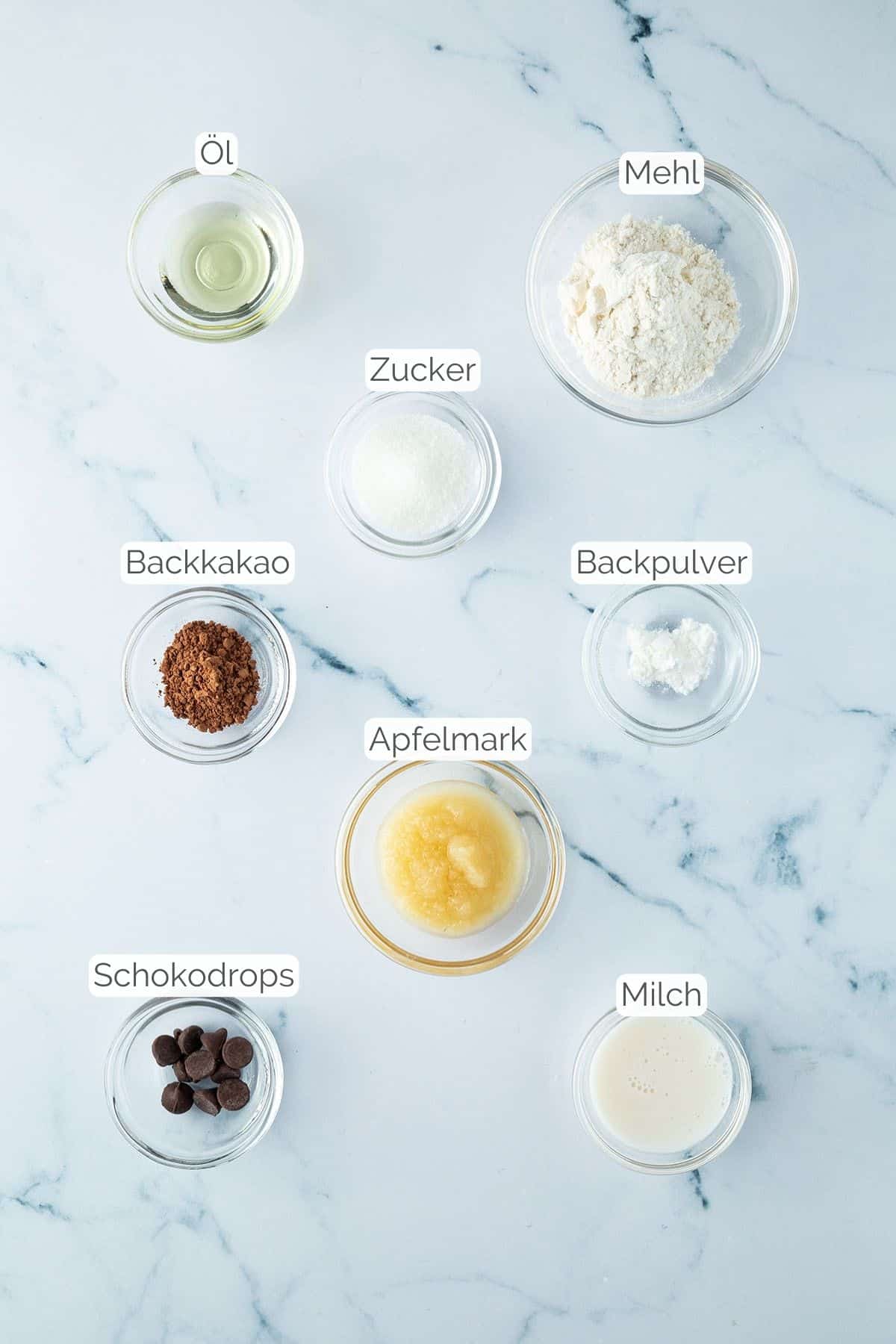 Alle Zutaten mit Textbeschriftungen, die für den Schoko-Tassenkuchen ohne Ei benötigt werden.