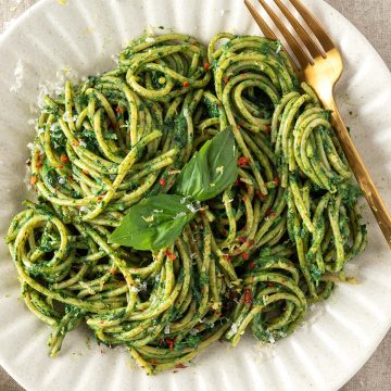 Ein gedeckter Tisch auf dem ein Teller mit Spaghetti mit gr&uuml;ner Sauce serviert werden.