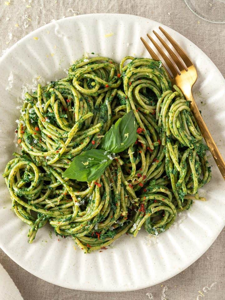 Ein gedeckter Tisch auf dem ein Teller mit Spaghetti mit gr&uuml;ner Sauce serviert werden.