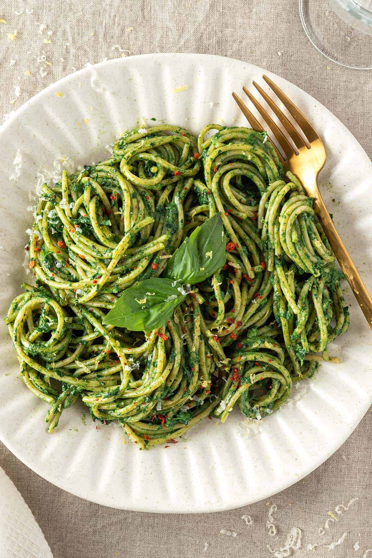 Ein gedeckter Tisch auf dem ein Teller mit Spaghetti mit gr&uuml;ner Sauce serviert werden.