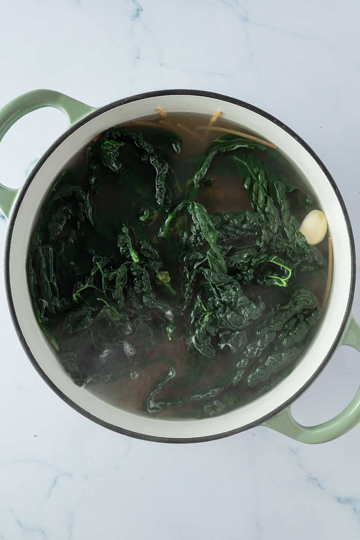 Ein Topf in dem Spaghetti, Schwarzkohl und eine Knoblauchzehe in Wasser kochen.