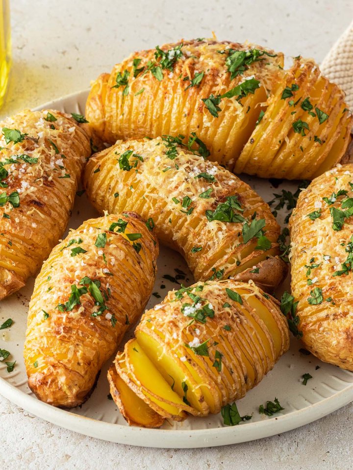 Knusprig gebackene F&auml;cherkartoffeln mit Parmesan und Petersilie auf einem Teller auf einem steinernen Hintergrund.