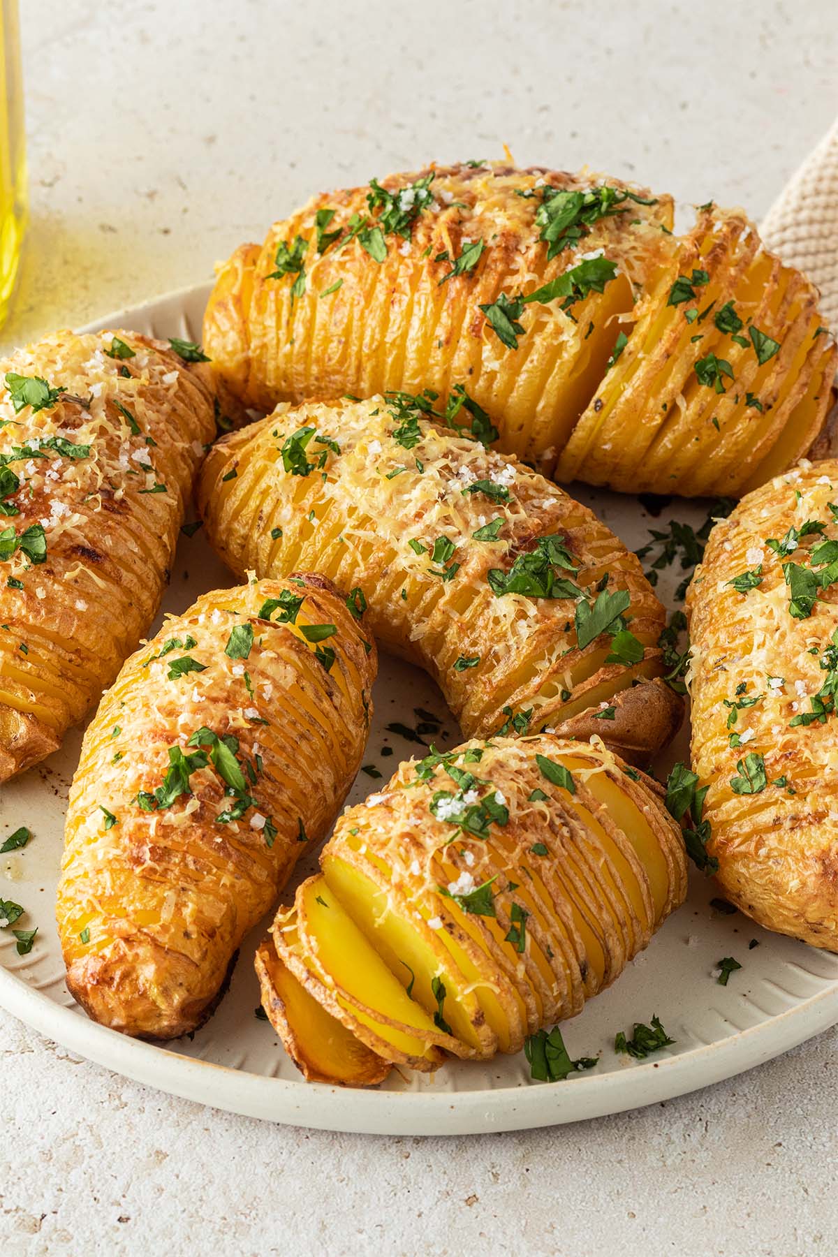 Knusprig gebackene F&auml;cherkartoffeln mit Parmesan und Petersilie auf einem Teller auf einem steinernen Hintergrund.