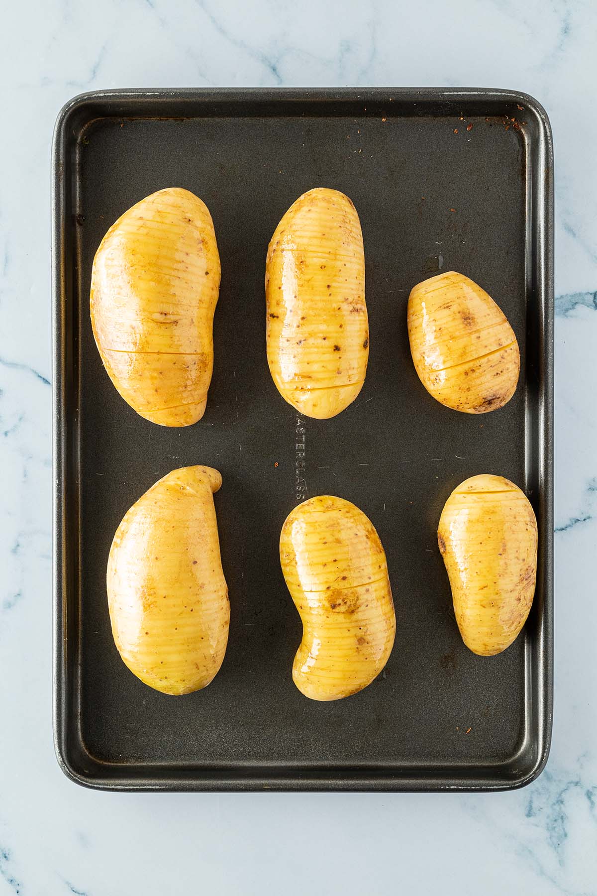 Eingeschnittene und mit &Ouml;l eingeriebene Kartoffeln auf einem Backblech.