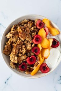 Weiches Granola in einer Sch&uuml;ssel mit Kirschen, Pfirsich und Joghurt.