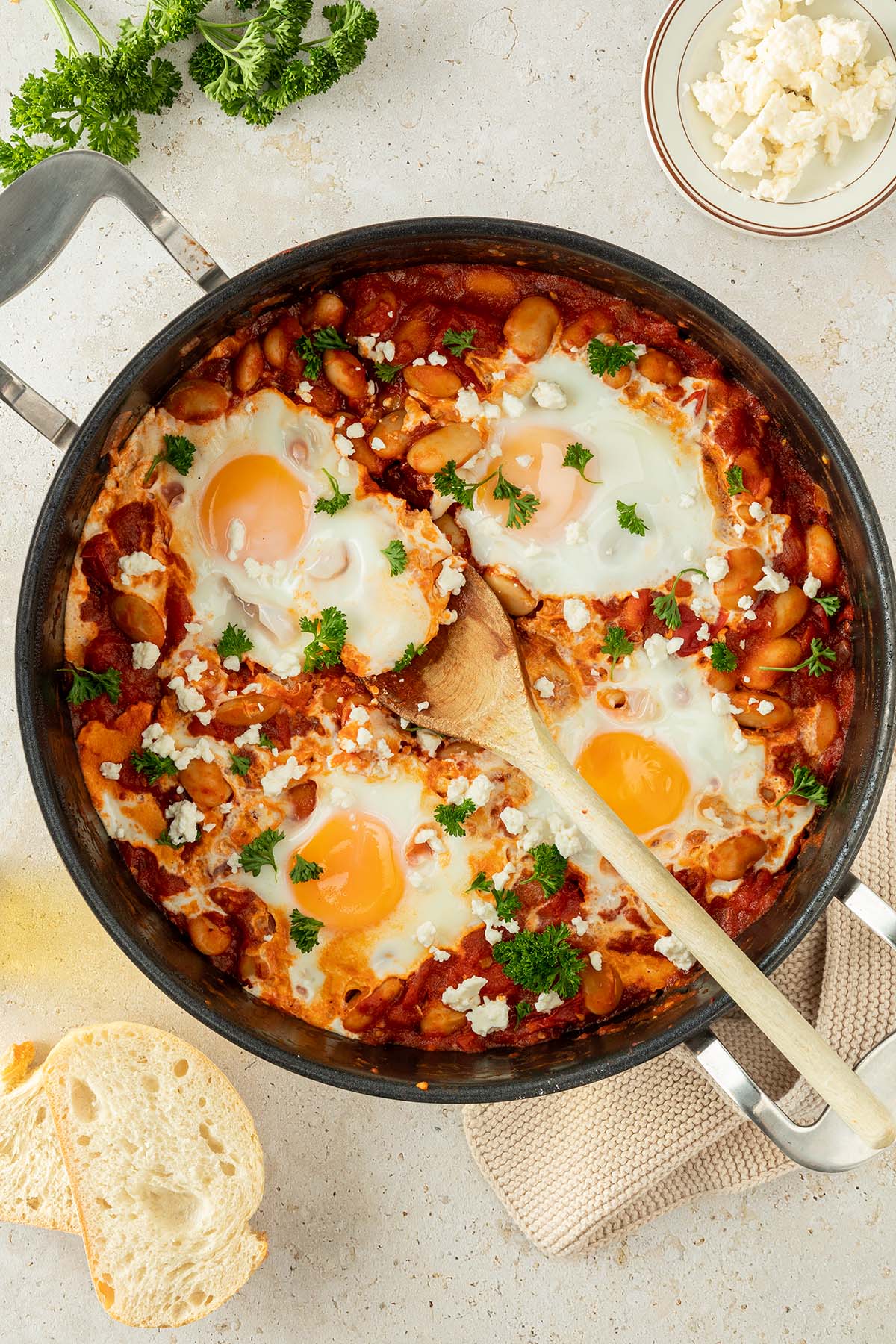 Vogelperspektive auf eine Pfanne mit Shakshuka, wo mit einem Kochl&ouml;ffel gerade eine Portion rausgenommen wird.