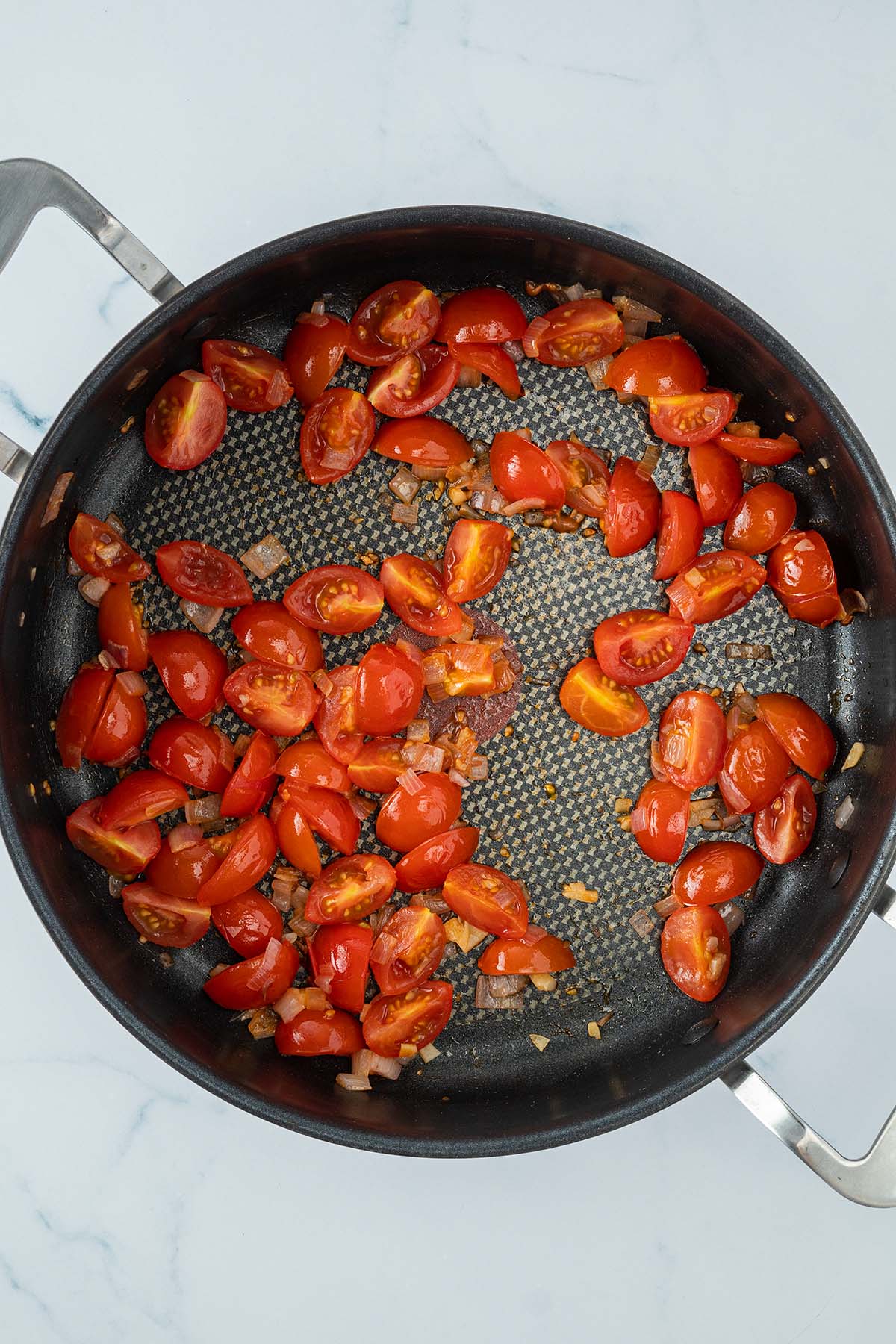 Weich angebratene Tomaten mit Zwiebeln und Knoblauch in einer Pfanne.