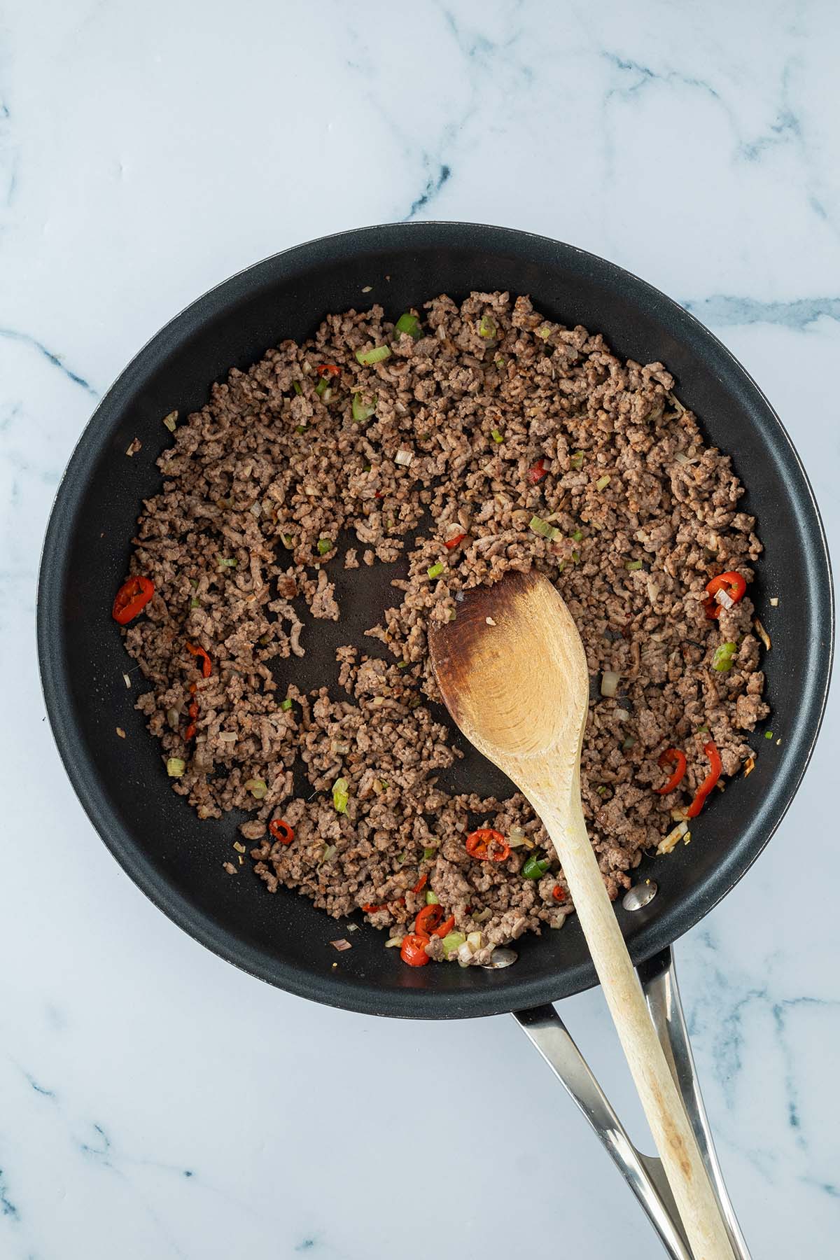 Vogelperspektive auf eine Pfanne mit kr&uuml;melig angebratenem Hackfleisch, Chili und Fr&uuml;hlingszwiebeln.