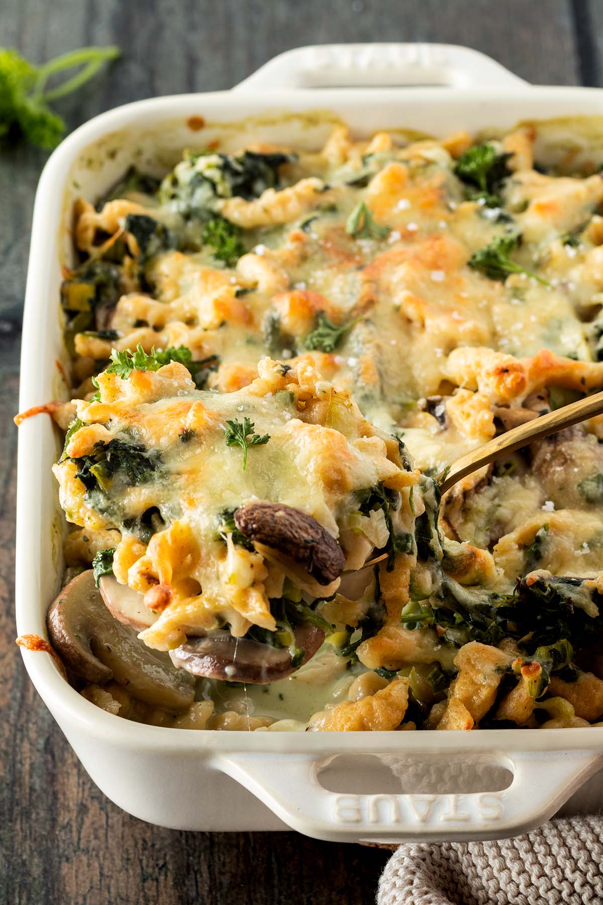 Nahaufnahme des Sp&auml;tzleauflaufs, w&auml;hrend eine Portion mit einem L&ouml;ffel rausgenommen wird.