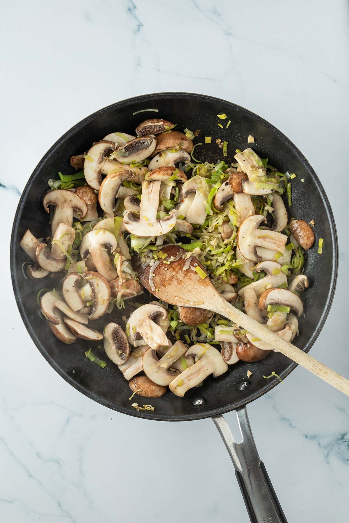 Lauch und Champignons werden in einer Pfanne angebraten.