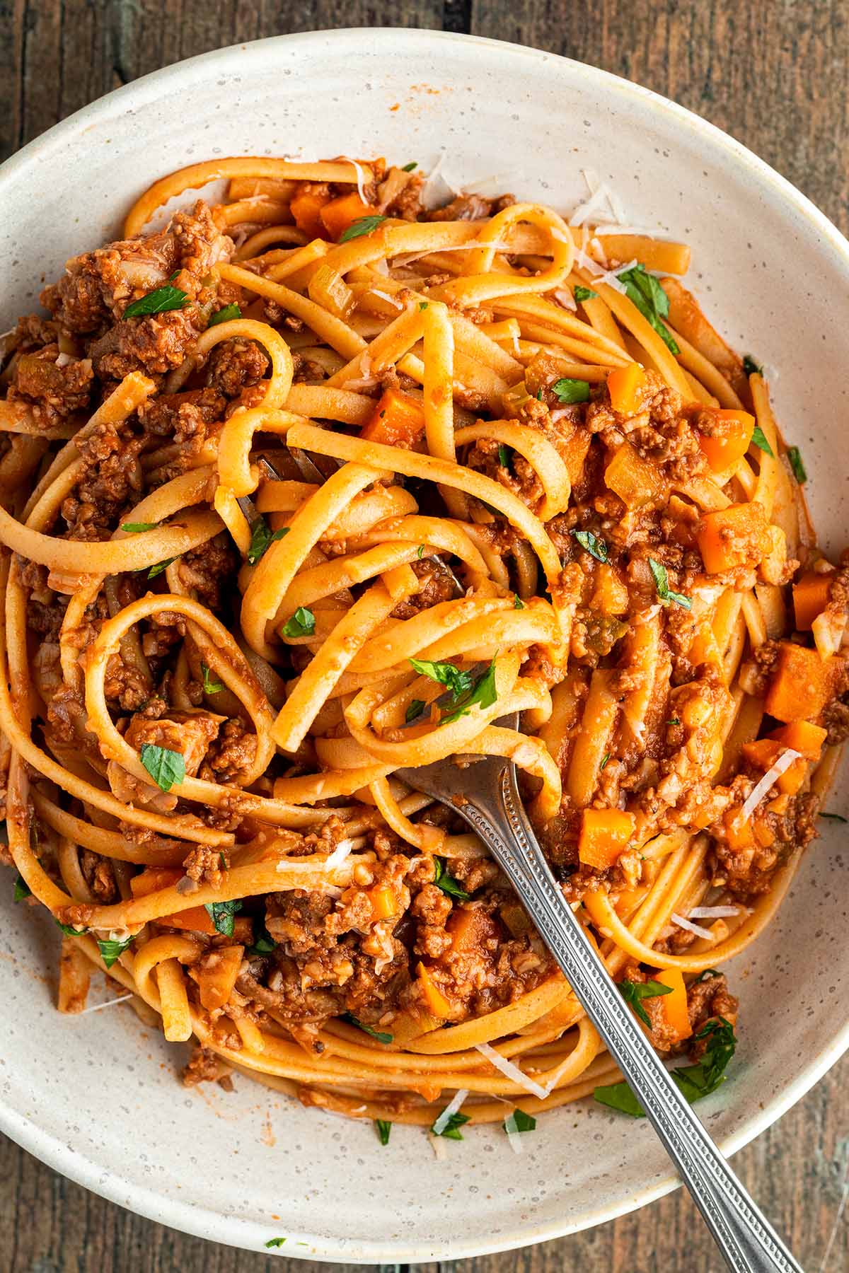 Teller mit Spaghetti Bolognese, wo eine Gabel einen Bissen Nudel aufgewickelt hat.