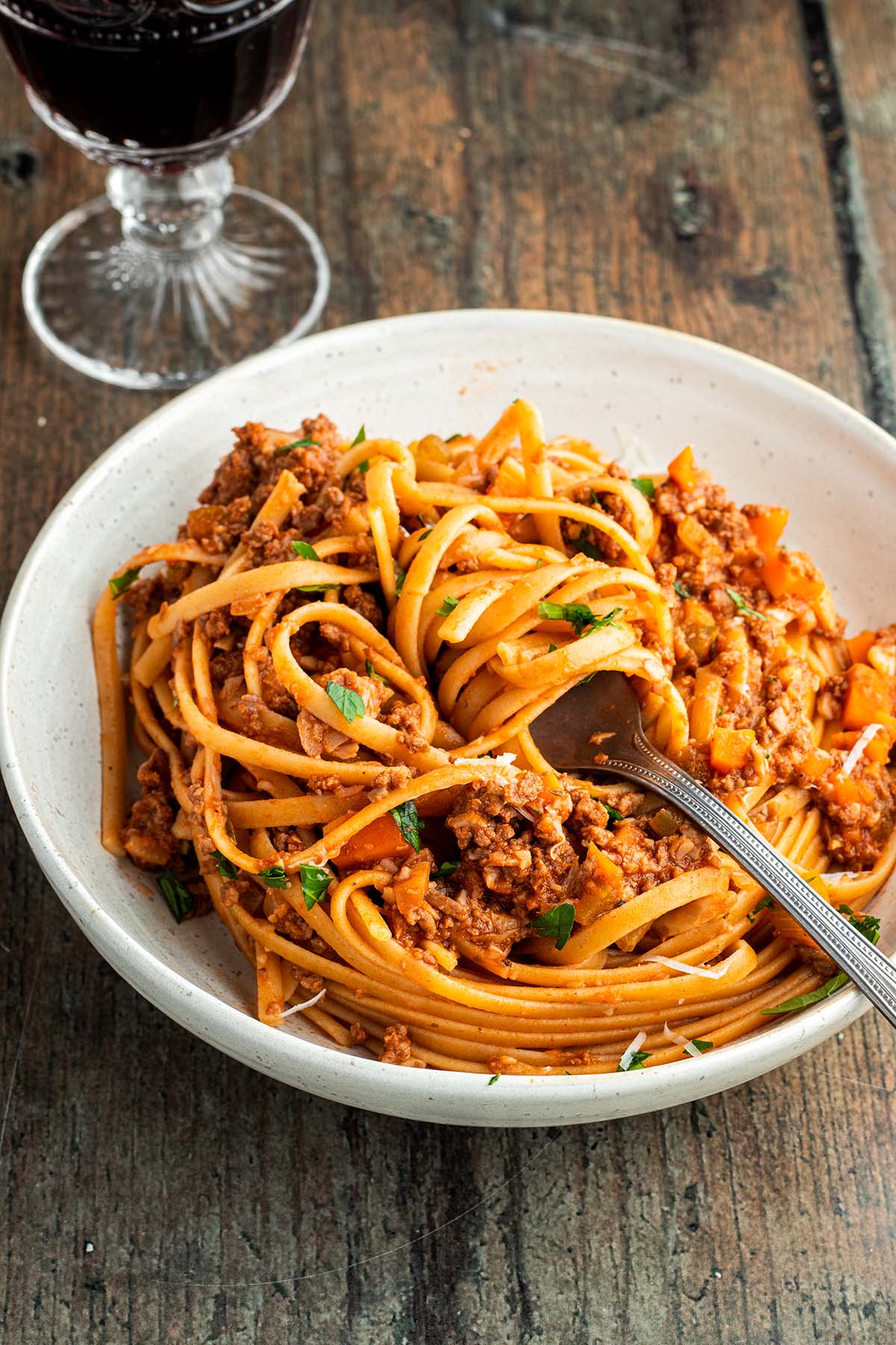 Ein Teller mit Spaghetti Bolognese und einem Glas Rotwein im Hintergrund.