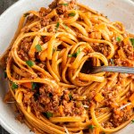 Teller mit Spaghetti Bolognese, wo ein Bissen Nudeln auf eine Gabel aufgewickelt wurden.