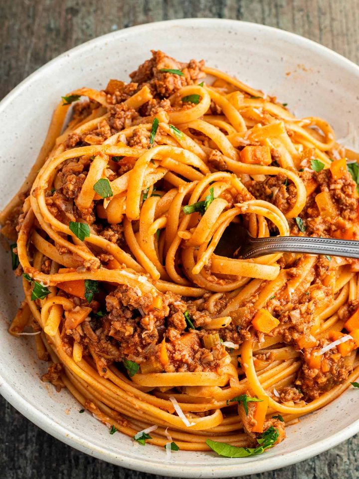 Teller mit Spaghetti Bolognese, wo ein Bissen Nudeln auf eine Gabel aufgewickelt wurden.