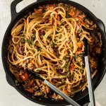 Spaghetti Puttanesca serviert in einer Gusseisenpfanne, Deko im Bildrand.