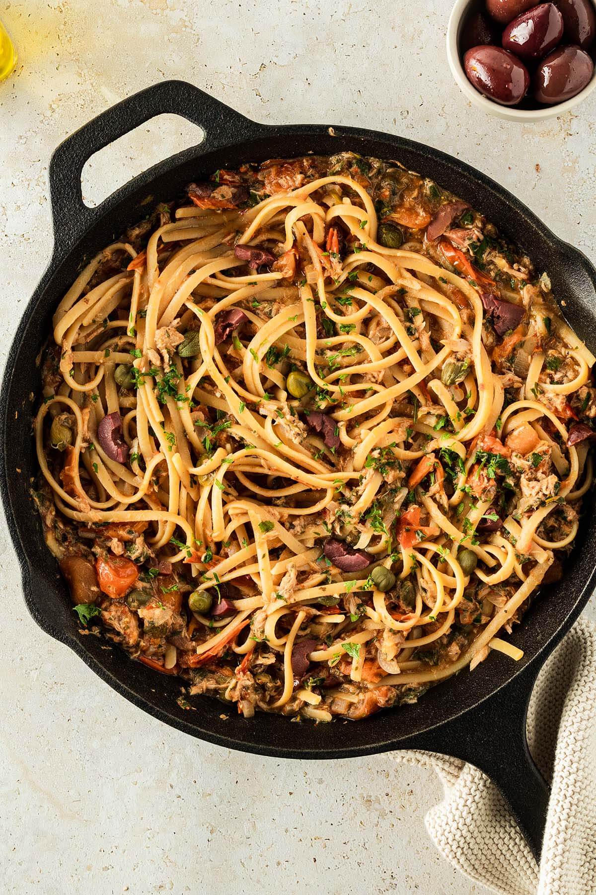 Spaghetti Puttanesca serviert in einer Gusseisenpfanne.