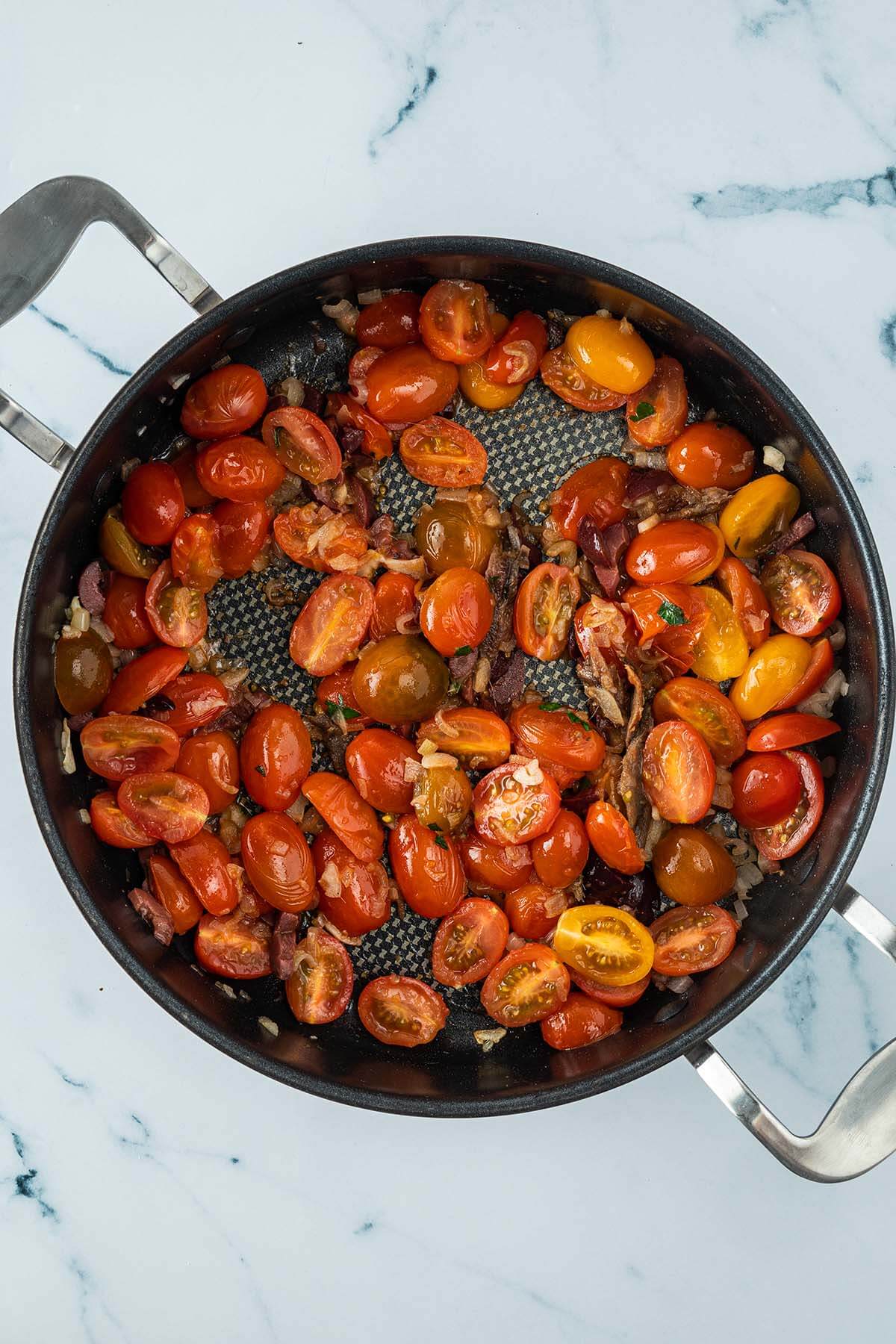 Vogelperspektive auf eine Pfanne mit weichen Tomatenh&auml;lften, Oliven und weiteren Zutaten.