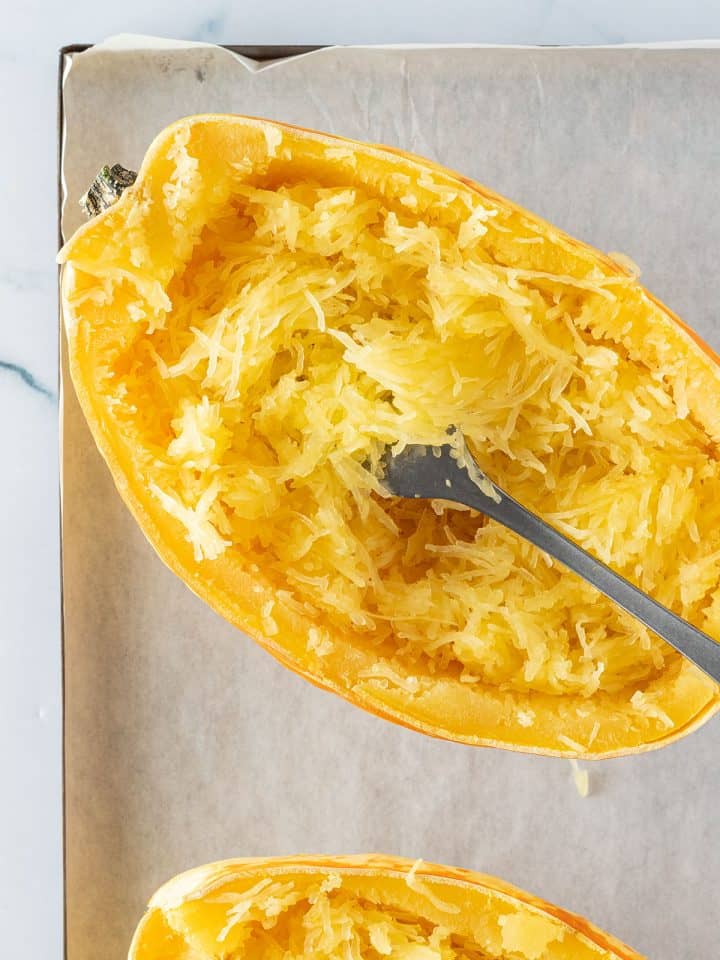 Ein halber Spaghettik&uuml;rbis auf einem Blech, wo das nudelf&ouml;rmige Fruchtfleisch mit einer Gabel aufgelockert wurde.