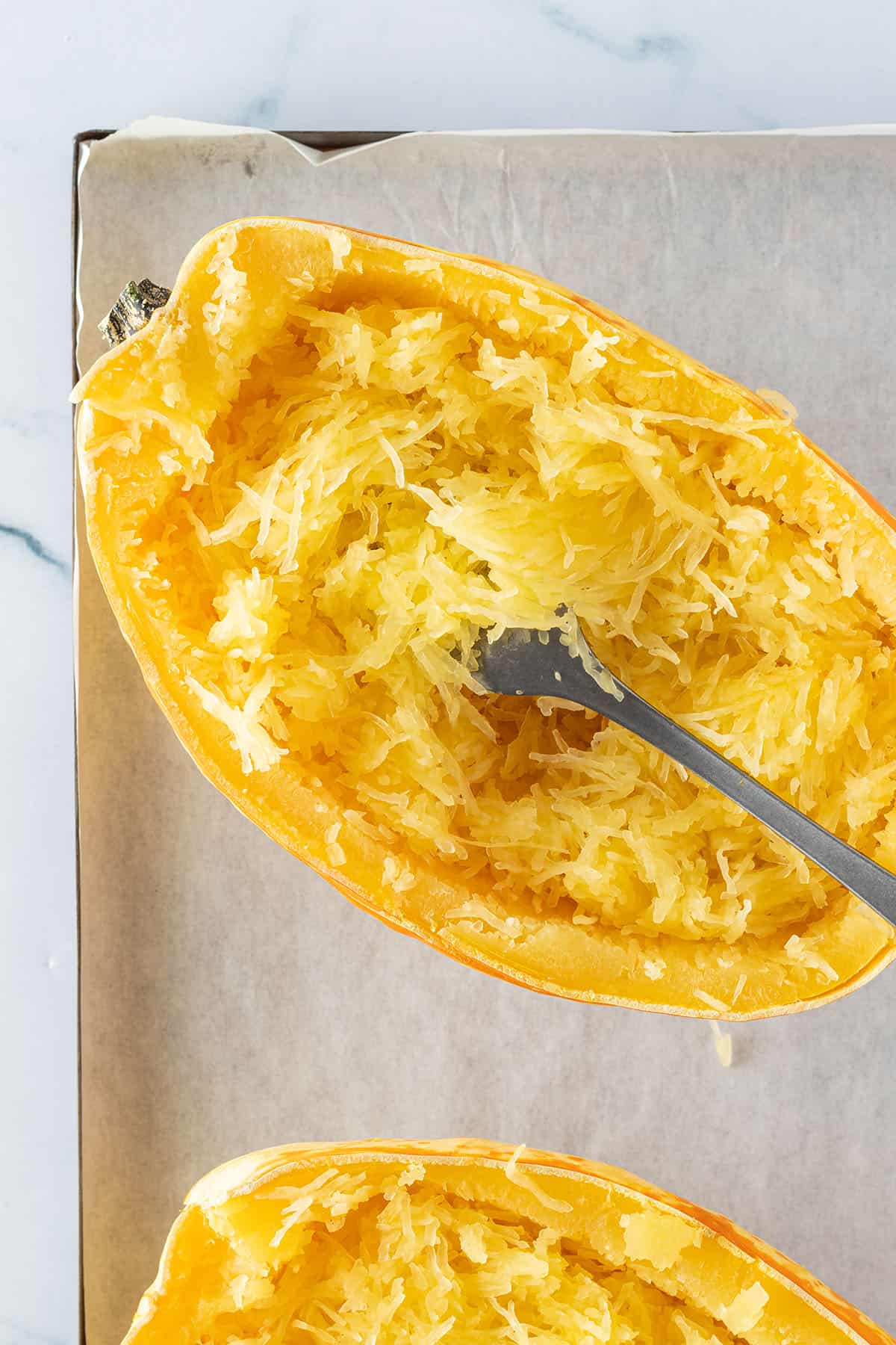 Ein halber Spaghettik&uuml;rbis auf einem Blech, wo das nudelf&ouml;rmige Fruchtfleisch mit einer Gabel aufgelockert wurde.