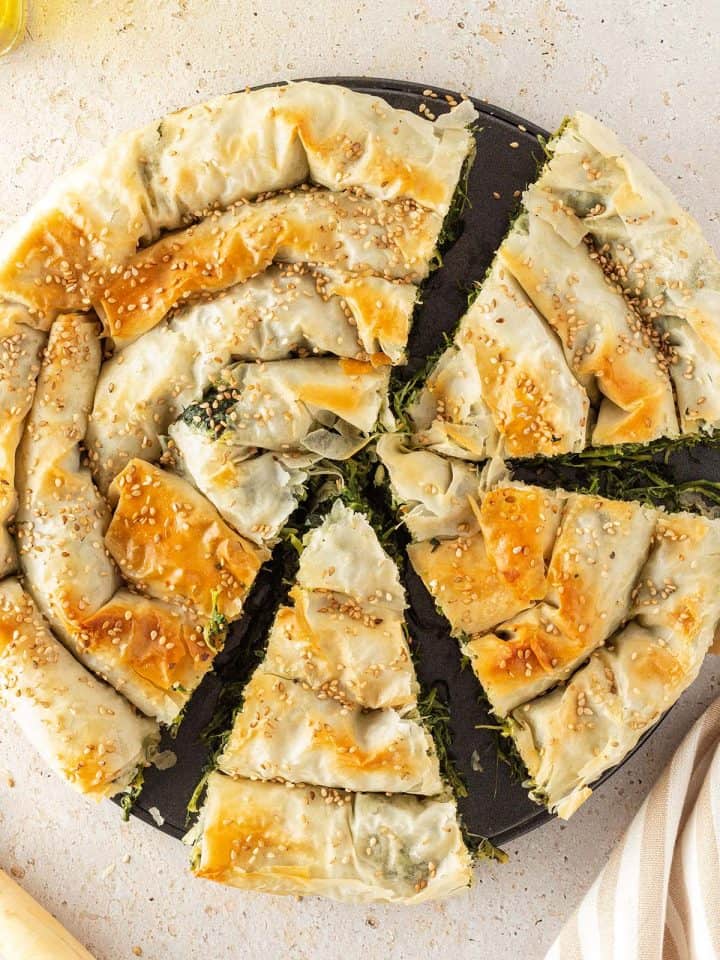 Goldbraun gebackener, griechischer Spinatstrudel, der zur H&auml;lfte angeschnitten ist.