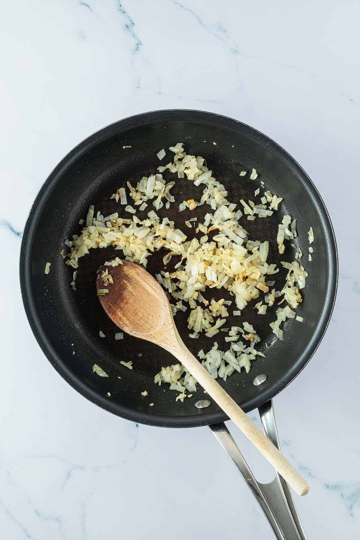 Glasig angebratene Zwiebel- und Knoblauchw&uuml;rfel in einer Pfanne.