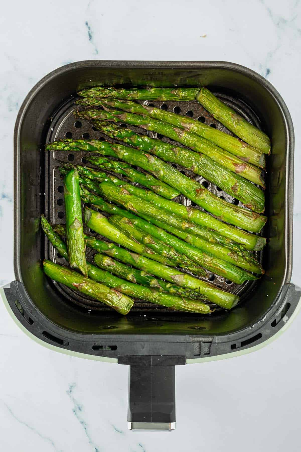 Gr&uuml;ner Spargel in dem Korb einer Hei&szlig;luftfritteuse.