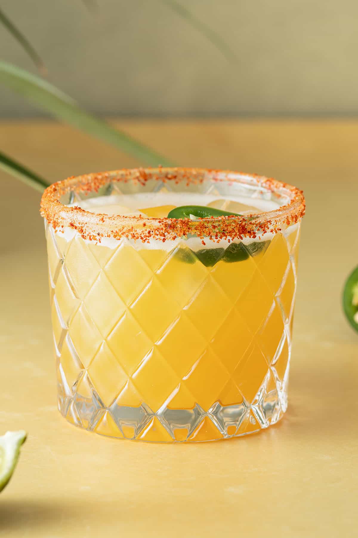Spicy Margarita Cocktail in einem Glas mit Chili-Salzrand und einer Jalape&ntilde;o-Scheibe auf einem gelben Untergrund.