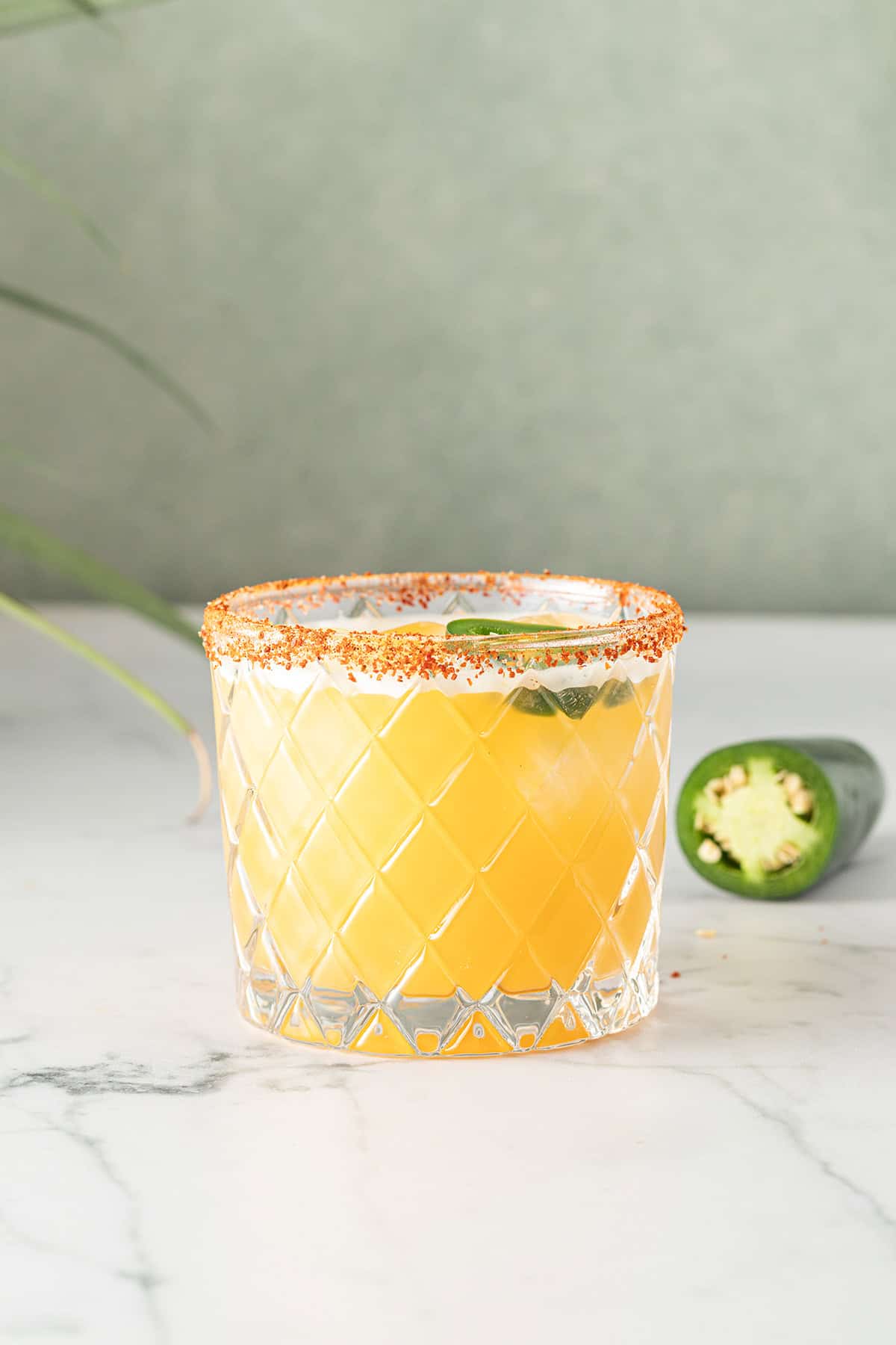Spicy Margarita Cocktail serviert in einem Glas mit Chili-Salzrand, eine angeschnittene Jalape&ntilde;o-Chili im Hintergrund.