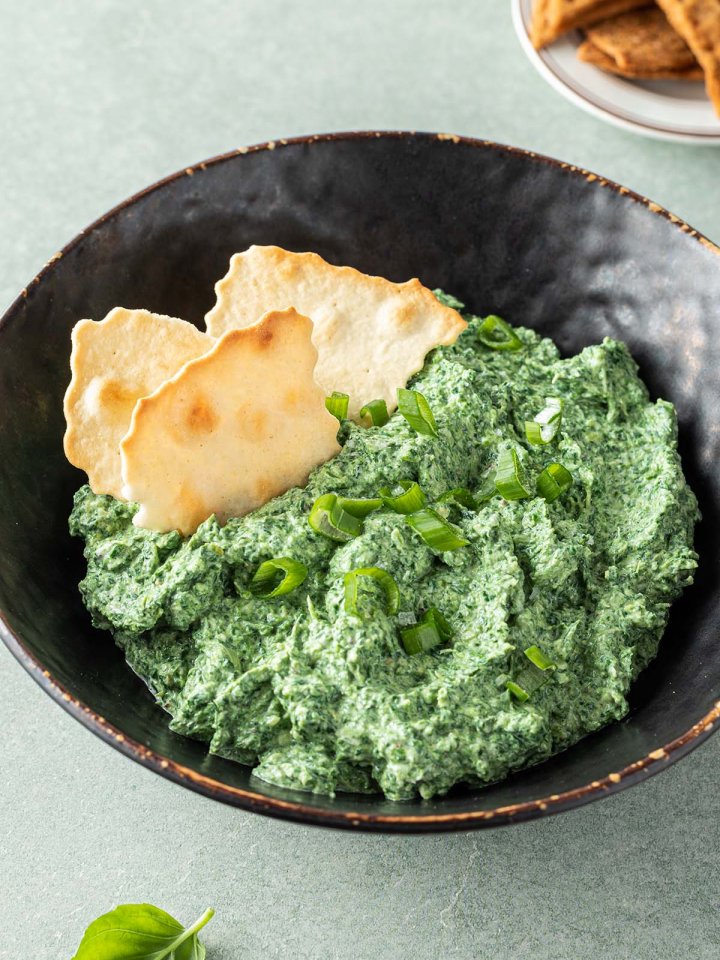 Cremiger Spinatdip in einer Sch&uuml;ssel mit Fr&uuml;hlingszwiebeln und Crackern serviert.