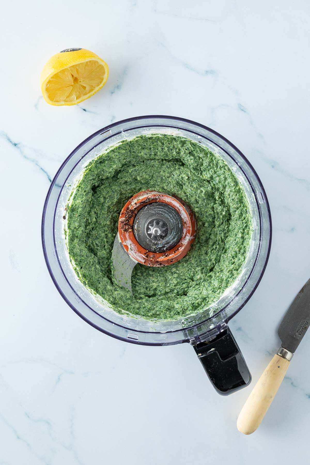 Spinat Dip in einem Food Processor mit einer ausgedr&uuml;ckten Zitrone daneben.