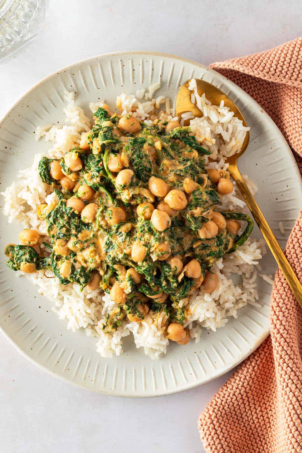 Eine Portion Spinat-Kichererbsen-Curry serviert auf Reis auf einem hellen, beigen Teller.
