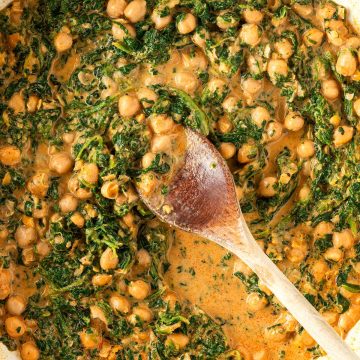 Fertiges Spinat-Kichererbsen-Curry in einer Pfanne mit einem Kochl&ouml;ffel.