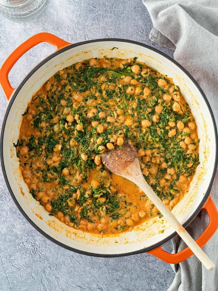 Eine Pfanne mit einem schnellen Spinat-Kichererbsen-Curry serviert auf einem grauen Untergrund.
