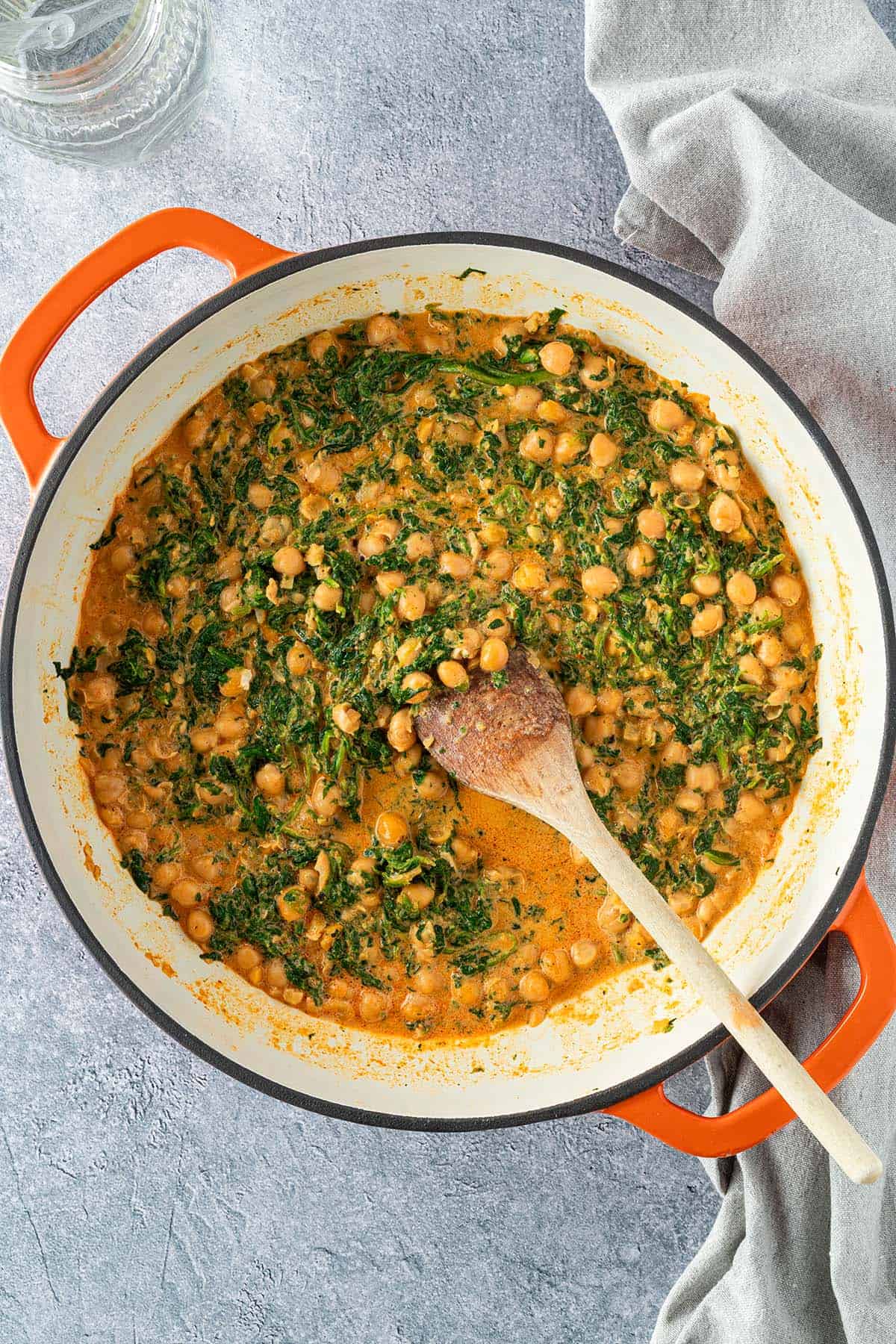 Eine Pfanne mit einem schnellen Spinat-Kichererbsen-Curry serviert auf einem grauen Untergrund.