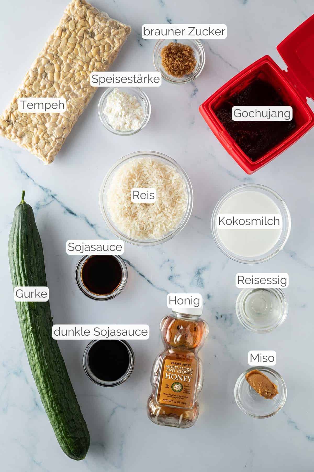 Alle Zutaten mit Textbeschriftungen, die f&uuml;r die Sticky Tempeh Bowl mit Kokosreis und Gochujang Gurkensalat ben&ouml;tigt werden.