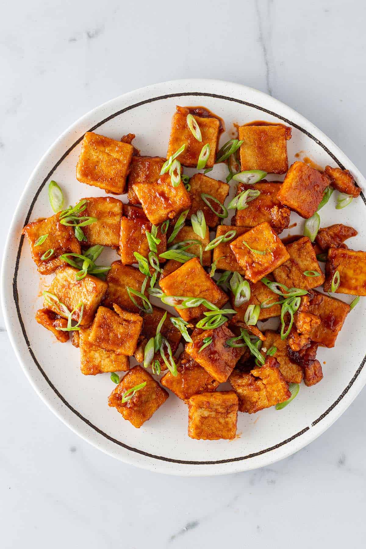 Knusprige Tofu-St&uuml;cke mit einer Sticky s&uuml;&szlig;-sauer Sauce auf einem Teller mit Fr&uuml;hlingszwiebeln.