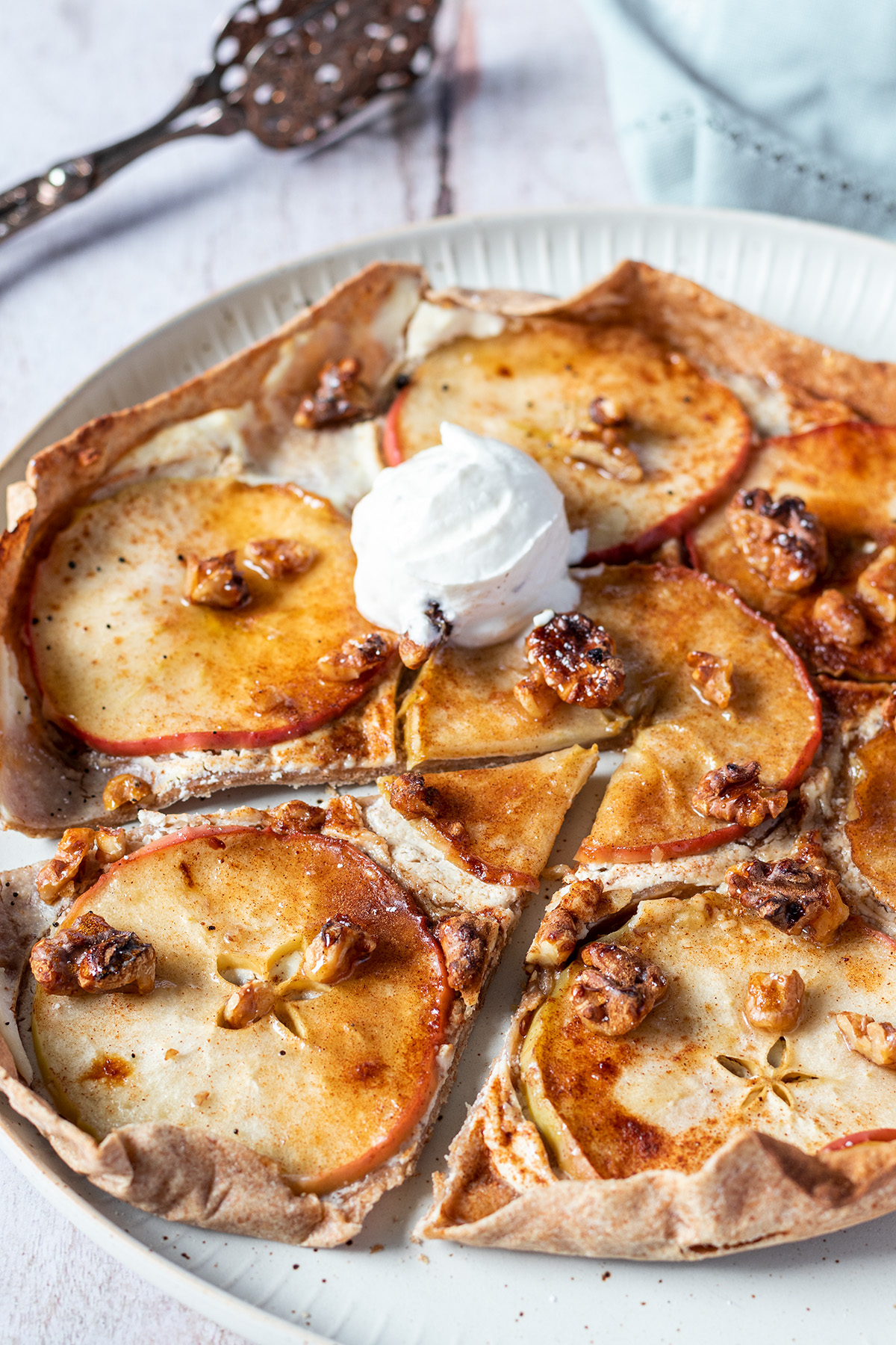 S&uuml;&szlig;er Flammkuchen mit in Scheiben geschnittenen &Auml;pfeln, Ricotta und Waln&uuml;ssen belegt und mit etwas Eis serviert.