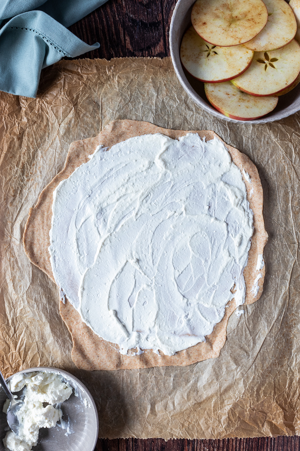 Rund ausgerollter Flammkuchenteig, der mit Ricotta bestrichen wurde auf, einem Backpapier.