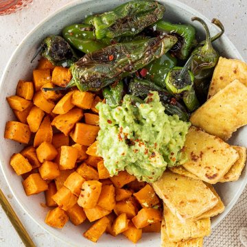 Sch&uuml;ssel mit S&uuml;&szlig;kartoffelw&uuml;rfel, angebratenen Pimientos, knusprigen Tofu-Scheiben und Guacamole in der Mitte.
