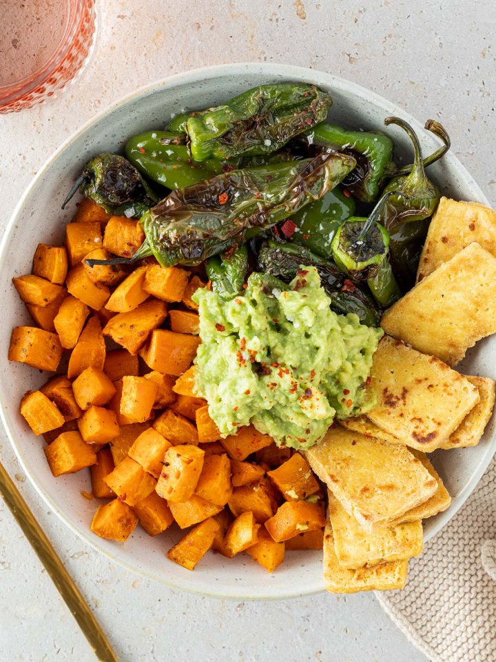 Sch&uuml;ssel mit S&uuml;&szlig;kartoffelw&uuml;rfel, angebratenen Pimientos, knusprigen Tofu-Scheiben und Guacamole in der Mitte.