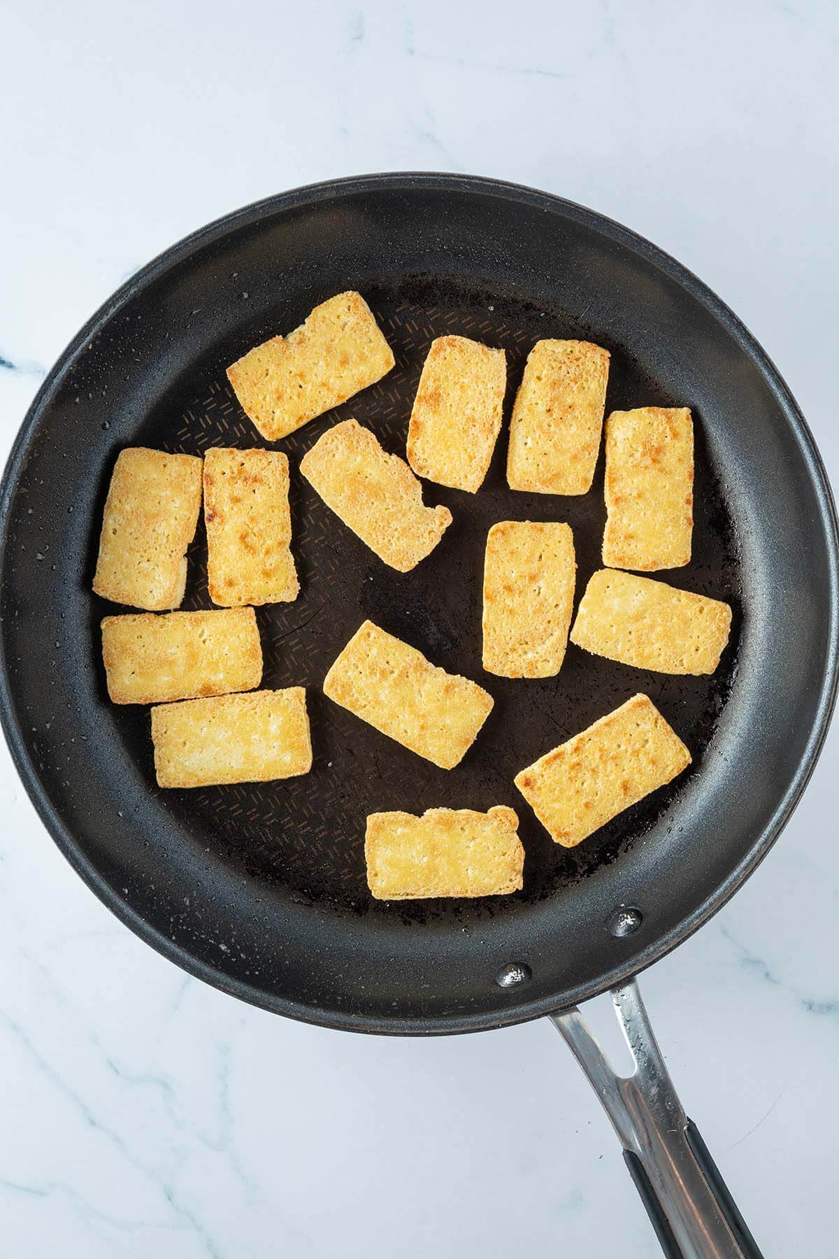 Knusprig, goldbraun angebratene Tofu-Scheiben in einer Pfanne.