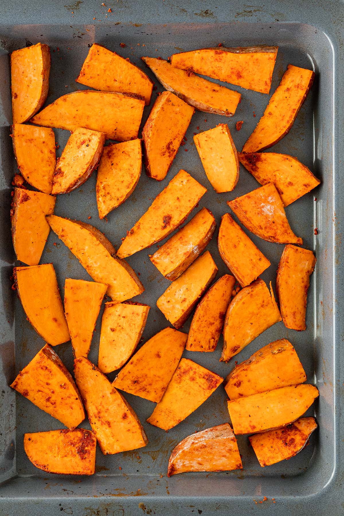 Rohe, gewürzte Süßkartoffelspalten auf einem Backblech.