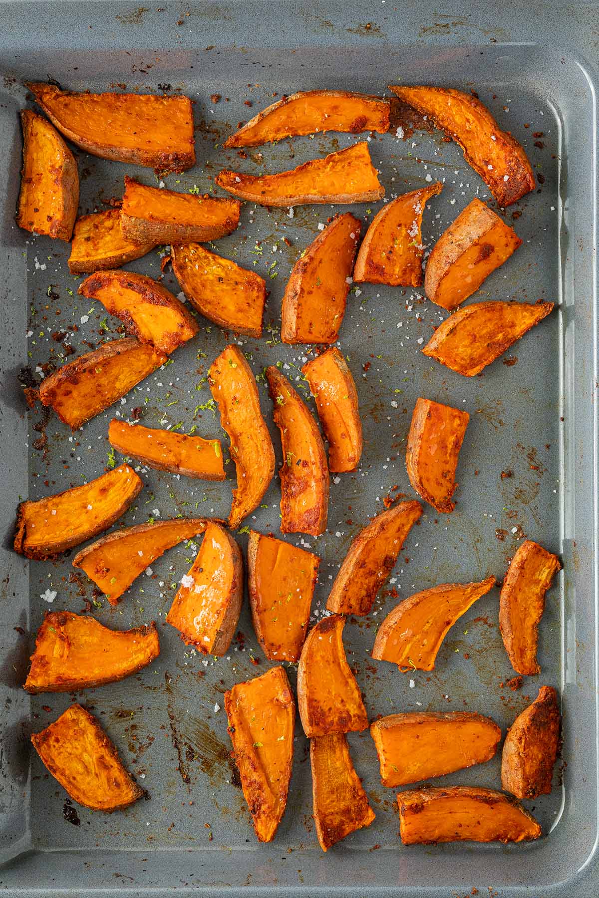 Knusprig gebackene Süßkartoffelspalten mit Salz und Limettenschale auf einem Backblech.